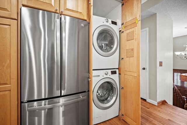 washroom with estacked washer and dryer, light wood finished floors, a chandelier, and baseboards