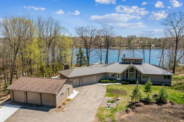 mid-century inspired home with a water view, metal roof, a front yard, an attached garage, and a view of trees