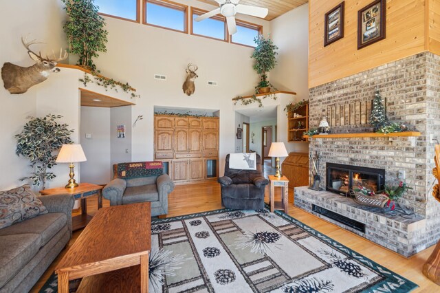 living room featuring a towering ceiling, ceiling fan, light wood finished floors, and a fireplace