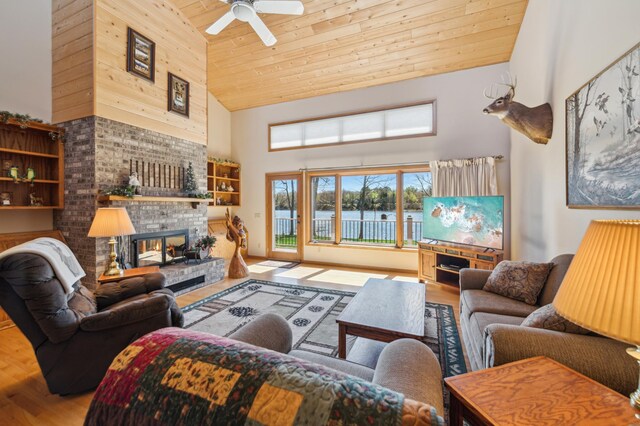 living area with high vaulted ceiling, wood ceiling, wood finished floors, a fireplace, and ceiling fan