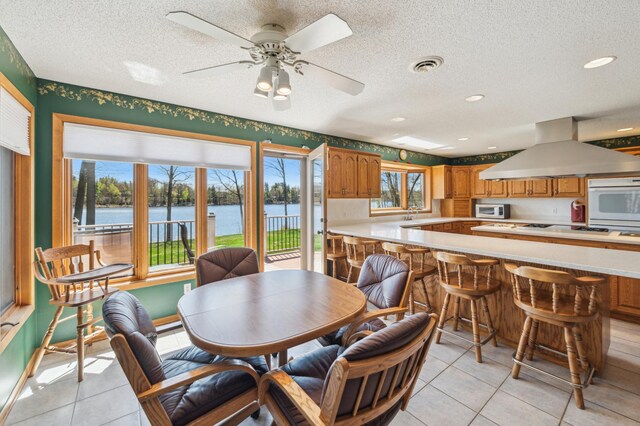 dining space with a textured ceiling, light tile patterned floors, a water view, recessed lighting, and a ceiling fan