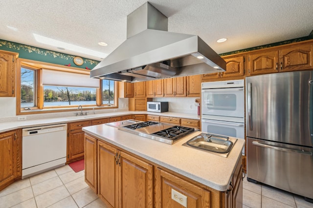 kitchen with stainless steel appliances, island exhaust hood, a textured ceiling, a sink, and a center island
