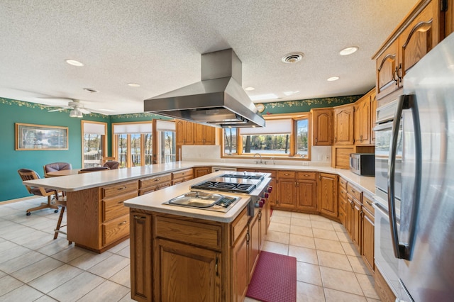 kitchen featuring island exhaust hood, a peninsula, stainless steel appliances, light countertops, and a textured ceiling