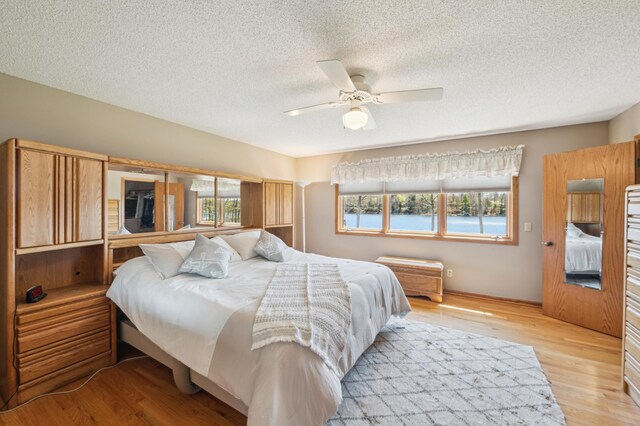 bedroom featuring multiple windows, a textured ceiling, light wood-style flooring, and ceiling fan
