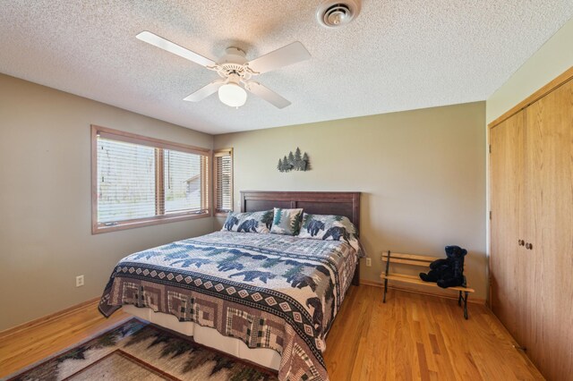 bedroom with a textured ceiling, a closet, light wood-type flooring, ceiling fan, and baseboards