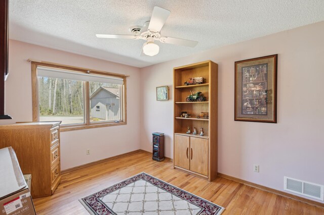 sitting room with light wood-type flooring, ceiling fan, baseboards, and a textured ceiling