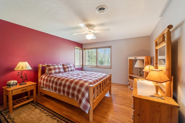 bedroom featuring light wood-type flooring, a textured ceiling, baseboards, and ceiling fan