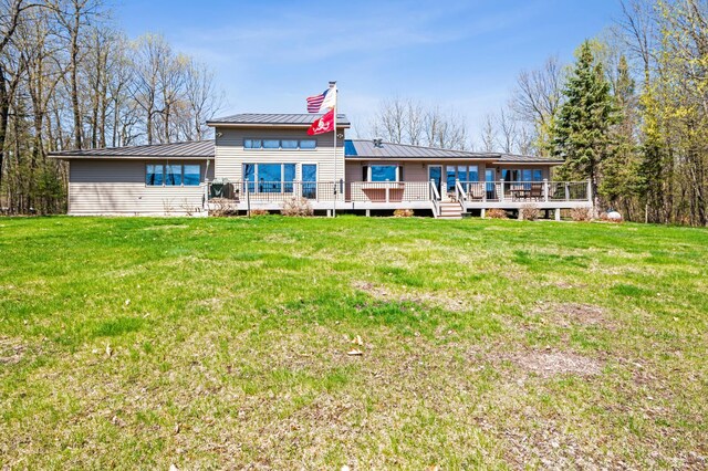 back of house with a wooden deck, a chimney, a yard, and metal roof