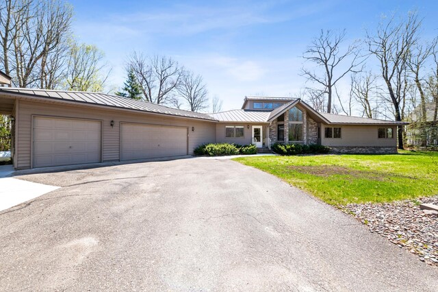view of front facade featuring asphalt driveway, a garage, a front lawn, stone siding, and metal roof