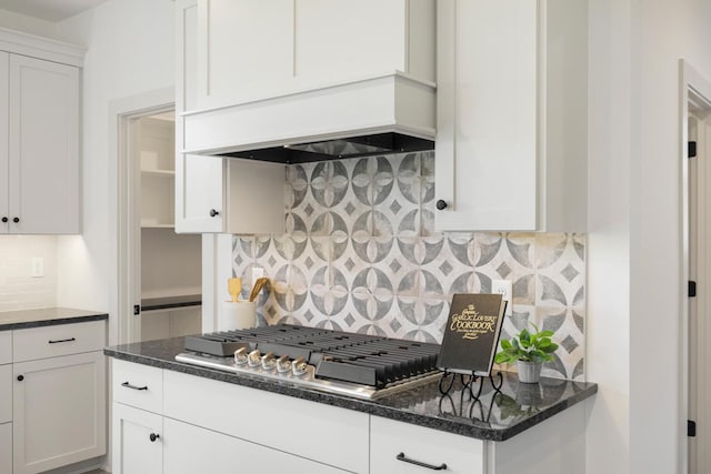 kitchen featuring stainless steel gas cooktop, dark stone countertops, white cabinetry, custom range hood, and tasteful backsplash