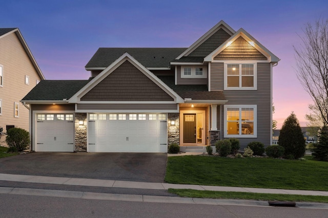 craftsman-style house featuring asphalt driveway, a lawn, an attached garage, and stone siding