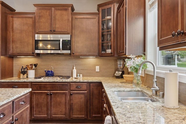 6573 Bridle Path, Corcoran, MN 55340 - kitchen featuring appliances with stainless steel finishes, a sink, decorative backsplash, glass insert cabinets, and light stone counters