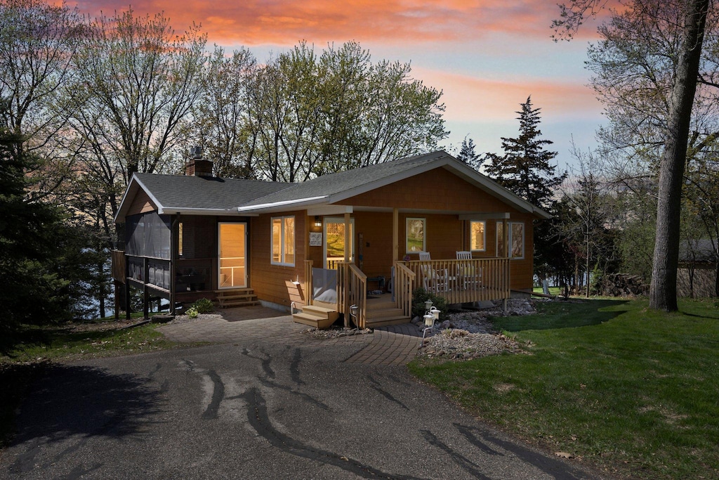 rustic home featuring a porch, aphalt driveway, a front lawn, and a chimney