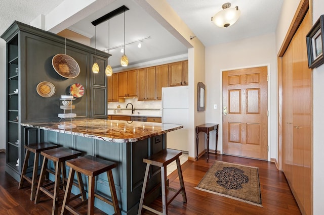 kitchen featuring freestanding refrigerator, a peninsula, dark stone counters, dark wood finished floors, and a breakfast bar area