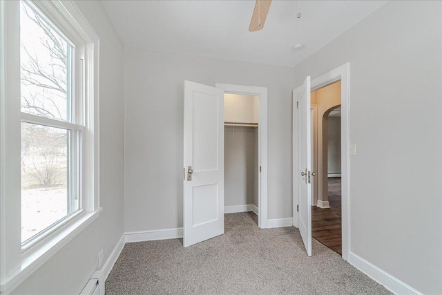 unfurnished bedroom featuring a ceiling fan, light colored carpet, baseboards, a closet, and a spacious closet