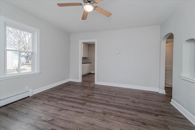 unfurnished room with a ceiling fan, arched walkways, dark wood finished floors, baseboards, and a baseboard heating unit