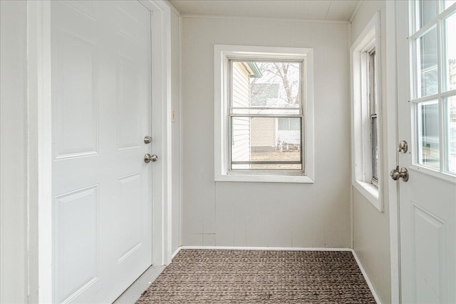 doorway to outside featuring crown molding, baseboards, light colored carpet, and a wealth of natural light