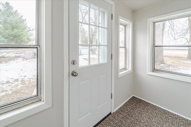 doorway to outside with crown molding, carpet floors, and baseboards