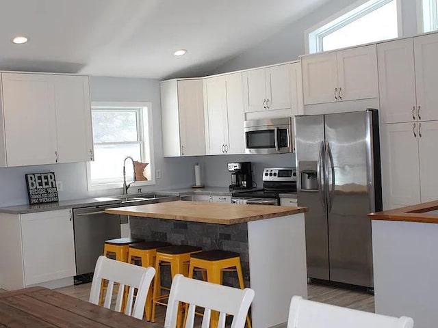 kitchen featuring white cabinets, a breakfast bar, stainless steel appliances, recessed lighting, and butcher block counters