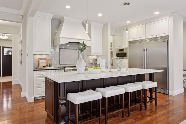 kitchen featuring appliances with stainless steel finishes, a center island with sink, a sink, white cabinets, and custom exhaust hood
