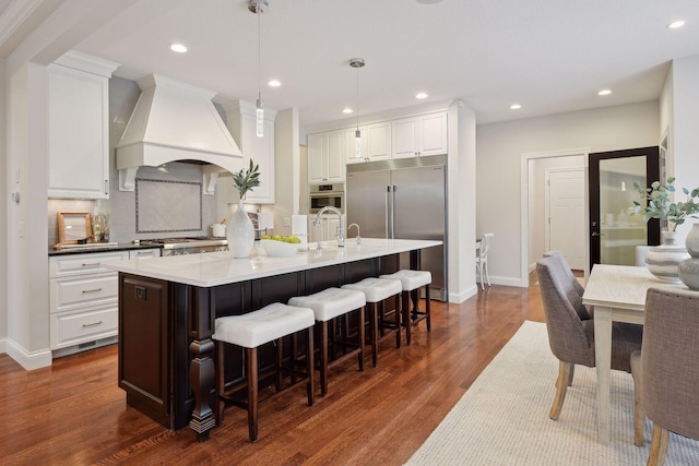 kitchen with dark wood-style flooring, built in fridge, white cabinetry, recessed lighting, and custom range hood