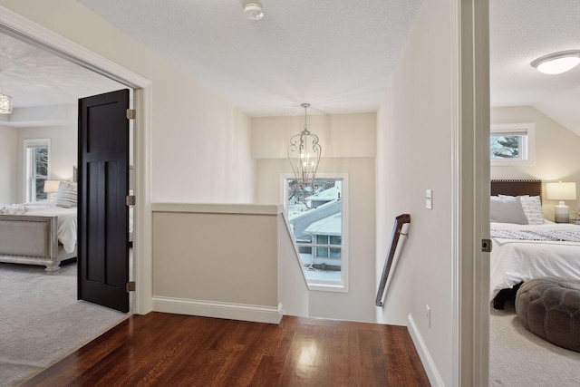 corridor featuring a textured ceiling, wood finished floors, baseboards, an upstairs landing, and an inviting chandelier