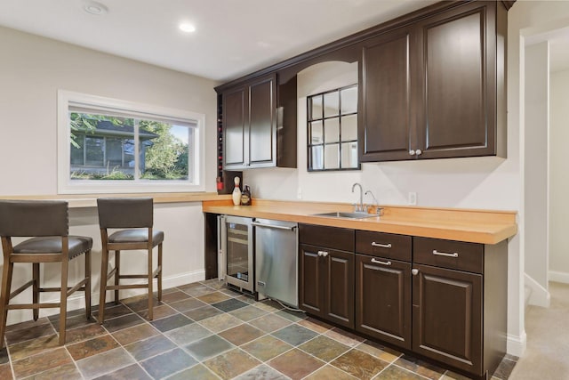 kitchen featuring dark brown cabinetry, a sink, dishwasher, baseboards, and wine cooler