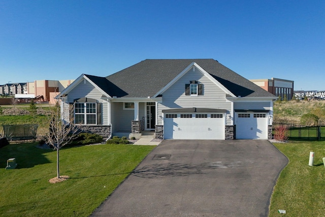 craftsman house featuring a front yard, fence, stone siding, and aphalt driveway