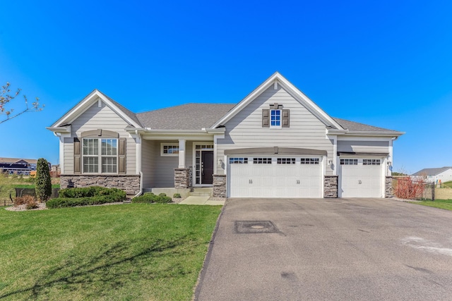 craftsman-style house featuring roof with shingles, a front yard, driveway, and stone siding