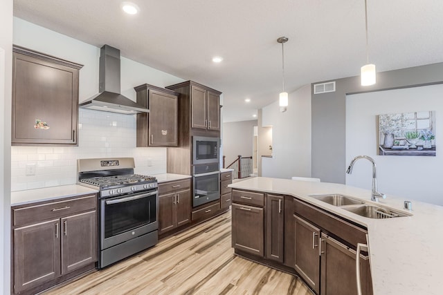 kitchen featuring a sink, light countertops, wall chimney exhaust hood, stainless steel appliances, and visible vents
