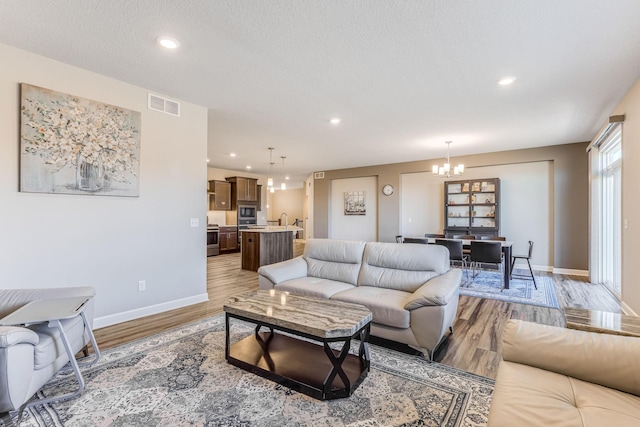 living room with visible vents, baseboards, recessed lighting, light wood-type flooring, and a notable chandelier