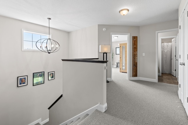 corridor with an upstairs landing, a chandelier, baseboards, carpet floors, and a textured ceiling