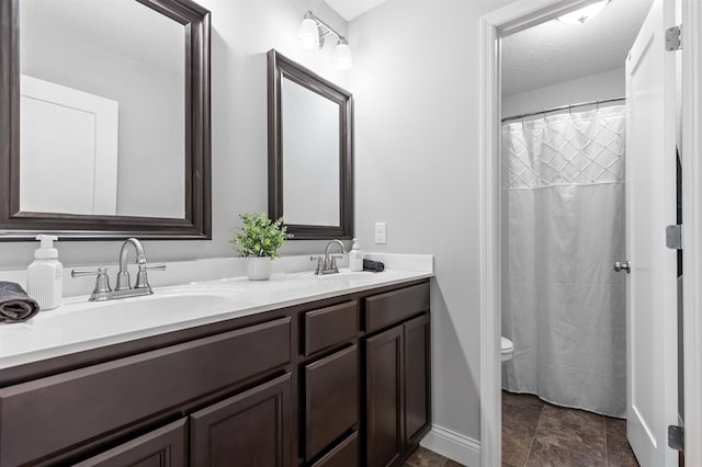 bathroom featuring double vanity, baseboards, a textured ceiling, and toilet