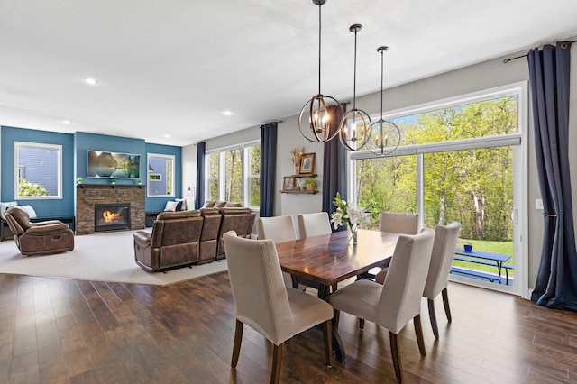 dining area featuring a chandelier, dark wood-style floors, a stone fireplace, and recessed lighting