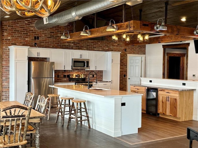 kitchen featuring brick wall, beverage cooler, an island with sink, a sink, and appliances with stainless steel finishes