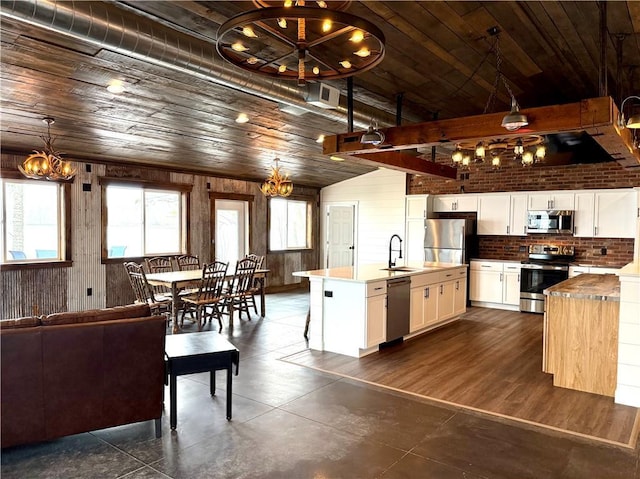 kitchen with wooden walls, a notable chandelier, appliances with stainless steel finishes, and a sink