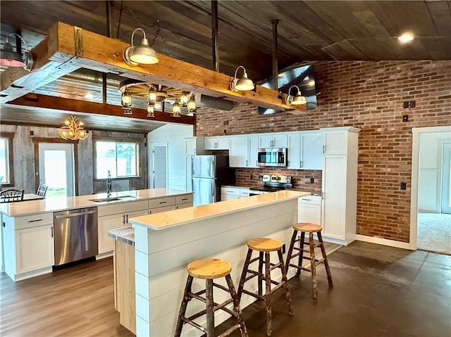 kitchen featuring brick wall, appliances with stainless steel finishes, a sink, white cabinetry, and an island with sink