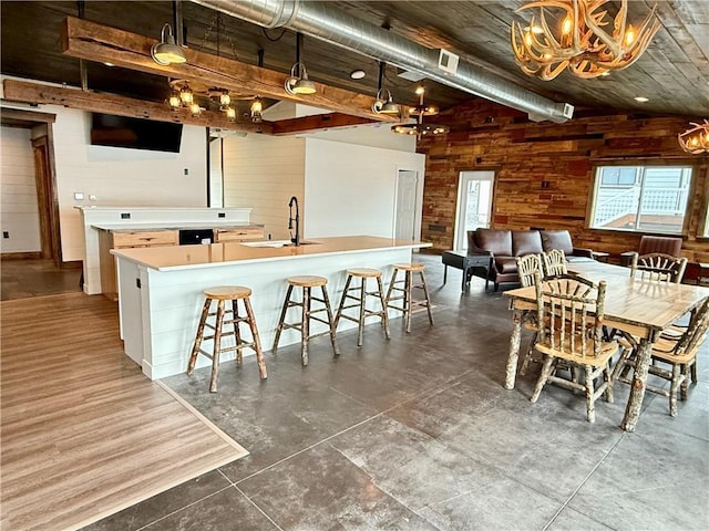 kitchen with wooden walls, light countertops, a large island with sink, a sink, and a notable chandelier