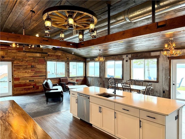 kitchen featuring stainless steel dishwasher, wood walls, vaulted ceiling with beams, a sink, and a notable chandelier