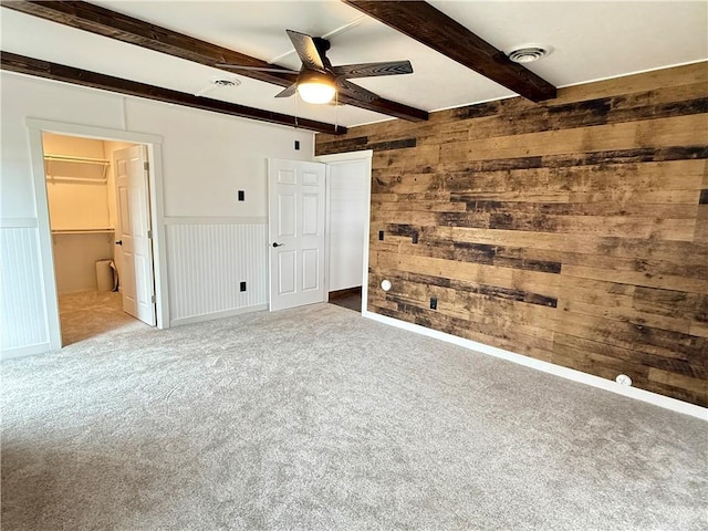 unfurnished bedroom featuring a closet, beamed ceiling, wooden walls, a spacious closet, and carpet flooring