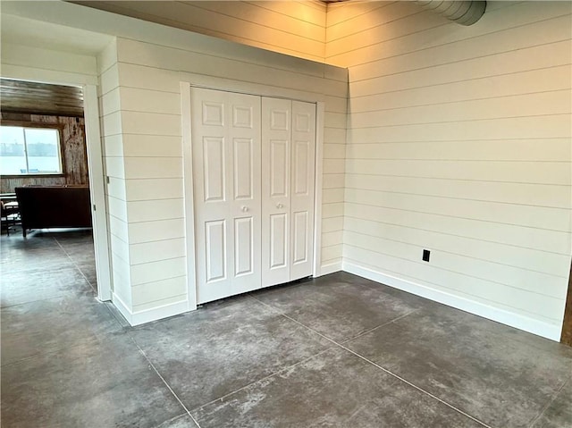 unfurnished bedroom featuring wooden walls, baseboards, concrete floors, and a closet