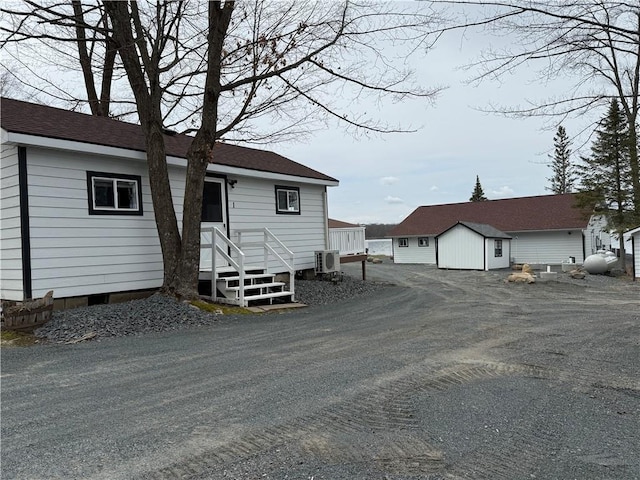 view of front of property with a storage shed, roof with shingles, an outbuilding, and central AC unit