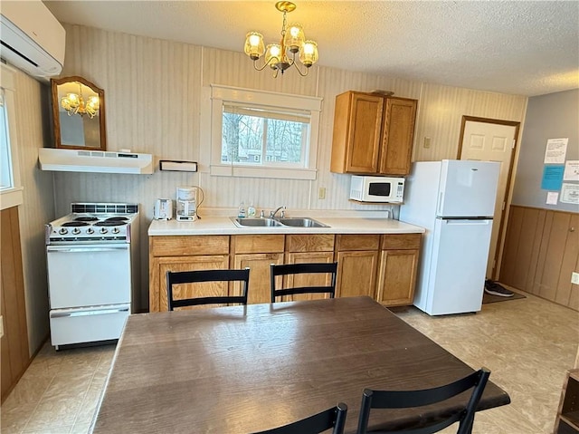 kitchen featuring an inviting chandelier, a sink, white appliances, under cabinet range hood, and a wall mounted AC