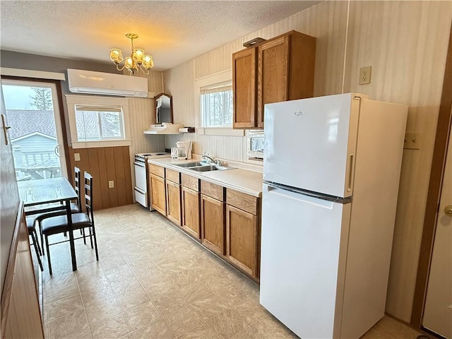 kitchen featuring brown cabinetry, white appliances, a wall unit AC, a sink, and a notable chandelier