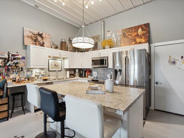 kitchen with stainless steel appliances, a kitchen breakfast bar, white cabinets, light countertops, and a high ceiling