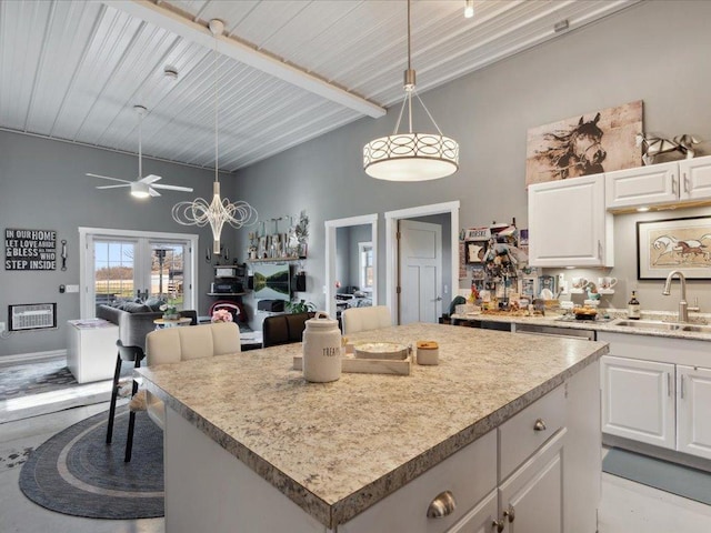 kitchen featuring a sink, white cabinetry, a towering ceiling, and decorative light fixtures
