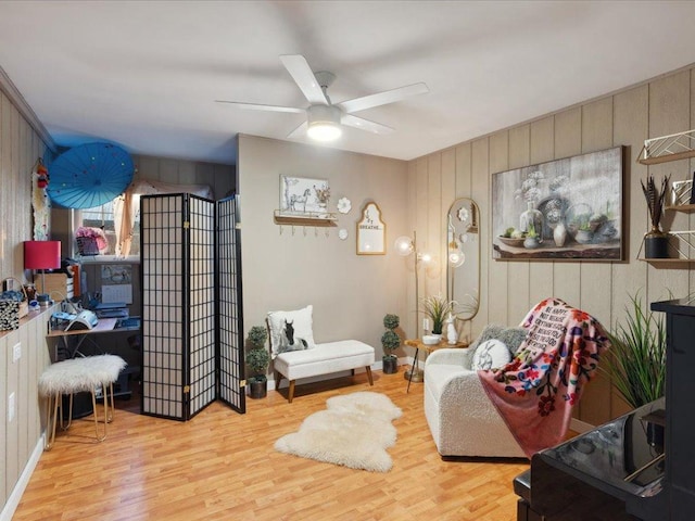 living area with a ceiling fan, wood finished floors, an office area, and wooden walls