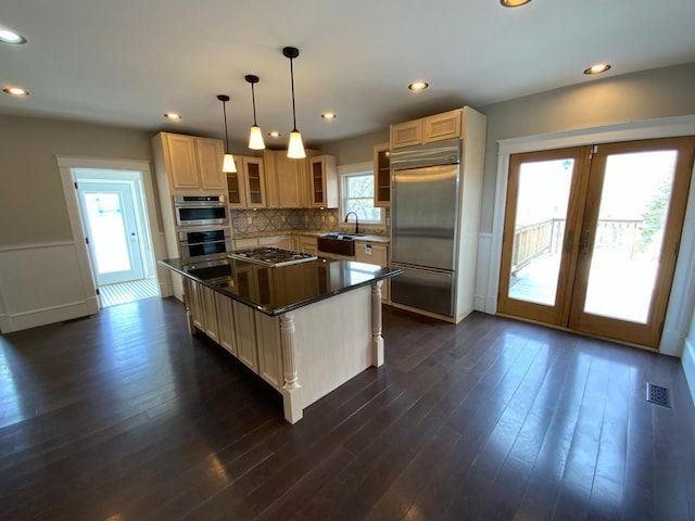 kitchen featuring appliances with stainless steel finishes, a sink, decorative backsplash, a kitchen island, and glass insert cabinets