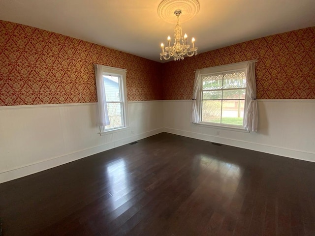 spare room with dark wood-style flooring, wallpapered walls, a notable chandelier, and a wainscoted wall