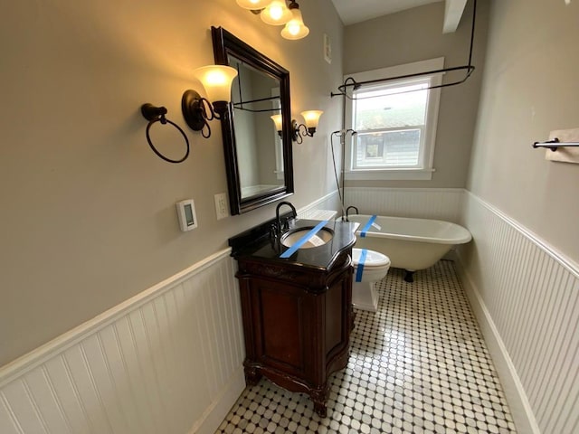full bathroom with vanity, a freestanding tub, a wainscoted wall, and toilet